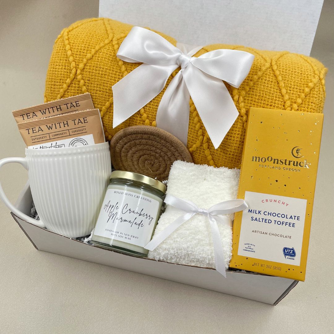 fall themed gift box with yellow blanket, fall scented candle, tea, mug and chcolate bar